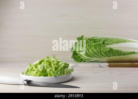 Cavolo cinese maturo intero e tagliato su tavola su fondo di legno bianco. Spazio per il testo Foto Stock