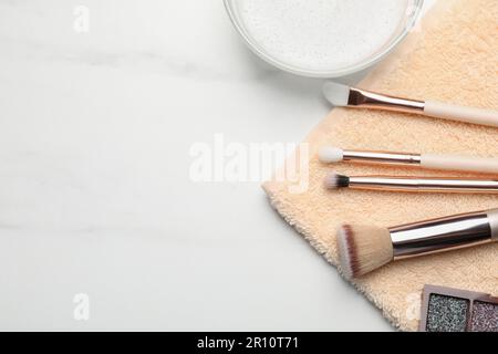 Pulire le spazzole per il trucco con un panno su un tavolo bianco, piatto. Spazio per il testo Foto Stock