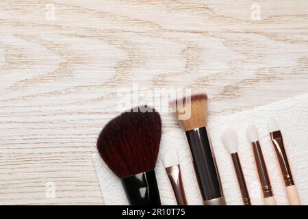 Pulire le spazzole per il trucco con un tovagliolo su un tavolo di legno, piatto. Spazio per il testo Foto Stock