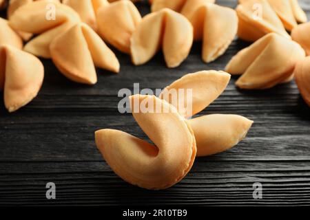 Biscotti gustosi della fortuna con le previsioni sul tavolo nero di legno, primo piano Foto Stock