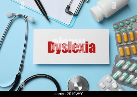 Carta con parola Dyslexia, stetoscopio, pillole e appunti su sfondo azzurro, piatto Foto Stock