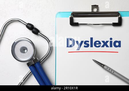 Clipboard con parola Dyslexia, penna e stetoscopio su tavolo bianco, piatto Foto Stock