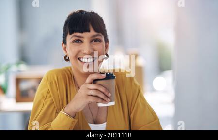 Questo buon umore è stato sponsorizzato dal caffè. Ritratto corto di una giovane e attraente donna d'affari seduta da sola nel suo ufficio e tenendo una tazza di caffè. Foto Stock