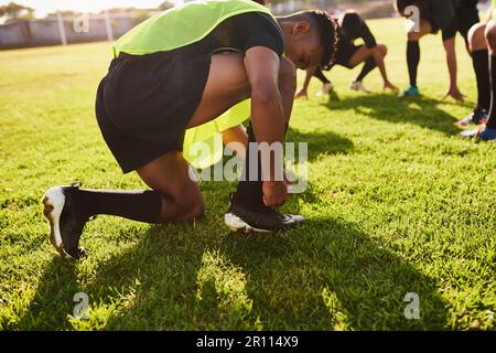 Questi devono essere legati prima di giocare. un bel giovane sportivo che legava le scarpe prima di giocare a rugby durante il giorno. Foto Stock