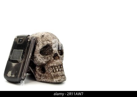il vecchio cellulare che poggia contro un cranio di metallo, il concetto di testing e la guida è pericoloso Foto Stock