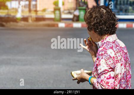Vista posteriore ritratto di donna anziana asiatica felice mangiare dolce frutta dura in mano sul lato della strada. La vecchia signora comprò un durian e mangiò delic durian fresco Foto Stock