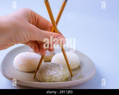 Chopsticks in mano di una donna che va a mangiare un tradizionale dessert giapponese mochi o daifuku in pasta di riso. Quattro palle di gelato mochi su piatto grigio su di Foto Stock
