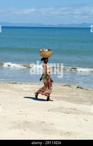 Donna locale sulla spiaggia di Nosy Be, che porta il cesto sulla sua testa, isola di Nosy Be, Madagascar, Nosy Be Foto Stock