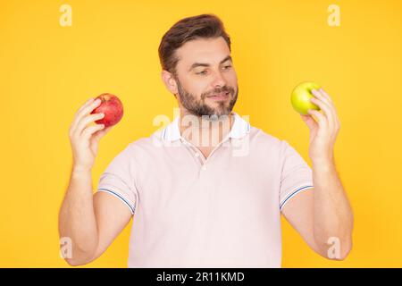 Uomo sorridente felice di mezza età che muta mela, stile di vita sano. L'uomo tiene un ritratto fresco verde mela studio su sfondo giallo isolato. Sano Foto Stock