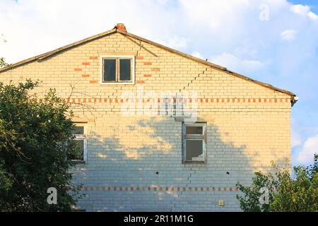 Una casa di mattoni bianchi a due piani con una crepa attraverso l'intera facciata contro un cielo blu in una primavera estate giorno. Edificio residenziale in mattoni bianchi con Foto Stock