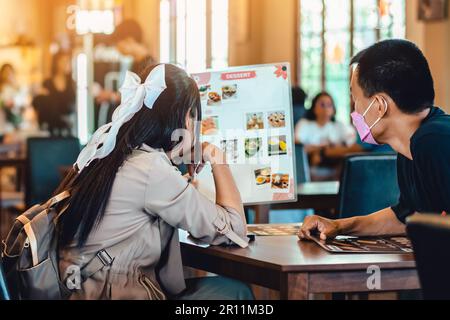 Vista posteriore del menu di lettura della giovane coppia asiatica e della scelta del pasto insieme. Il giovane amante ha letto una carta al ristorante mentre pranzava. Coppia di felicità lo Foto Stock