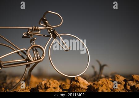 Una bicicletta in metallo in miniatura contro un cielo blu grigio scuro. Giocattolo falso souvenir fatto a mano mini moto artigianale in un selvaggio. Concetto di mountain bike. La ruota di un Foto Stock