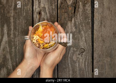 la mano tiene una tazza con gelato alla frutta e marmellata su sfondo di legno Foto Stock