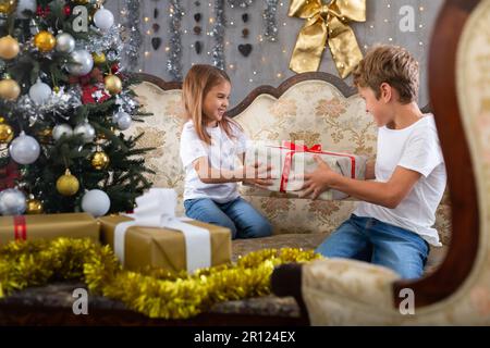 Bambina e ragazzo in casa con regalo in studio con interni natalizi Foto Stock