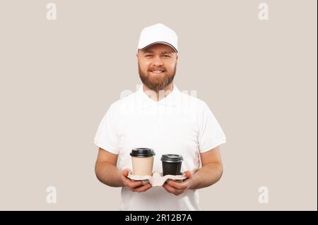 Il barista o il grande uomo sorridente che indossa una divisa bianca tiene due tazze di caffè da togliere. Foto Stock