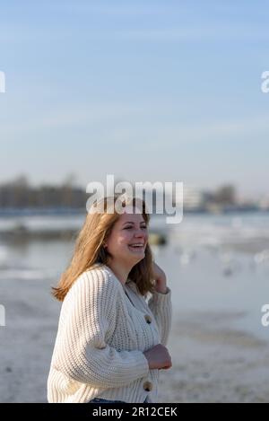 Giovane donna sorridente in maglione a maglia che corre in spiaggia Foto Stock