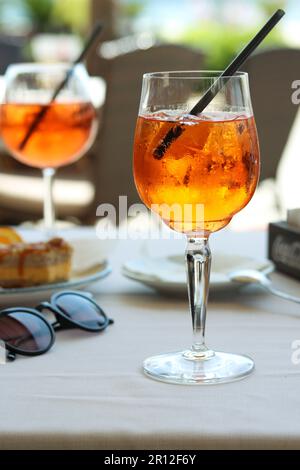 Un bicchiere di aperol spritz o un cocktail di arance campari con fetta d'arancia e ghiaccio sul tavolo del ristorante in riva al mare in una giornata di sole. Concetto di vacanza. S Foto Stock