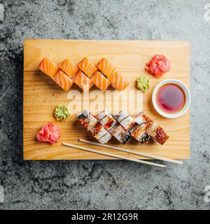 Uno shot di un tradizionale piatto di sushi servito su un asse di legno, completo di bastoncini Foto Stock