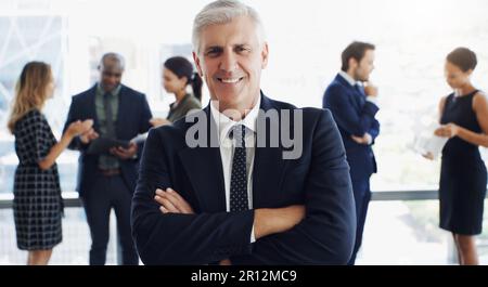 Il tuo unico concorso è chi eri ieri. un bel uomo d'affari sorridente alla fotocamera mentre i colleghi sono sfocati sullo sfondo. Foto Stock
