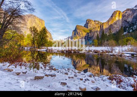 Uno splendido tramonto invernale illumina il tranquillo lago situato in un campo innevato circondato da maestose montagne rocciose Foto Stock