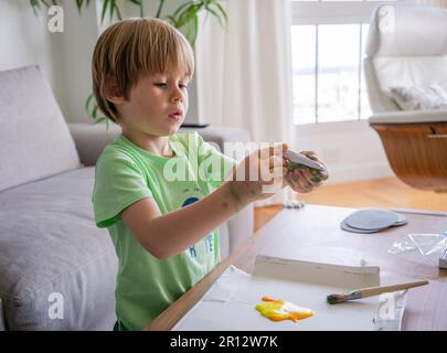 Giovane ragazzo dipingendo scritta verde decorativa su un sketchpad con un pennello e pittura a colori ad acqua. Foto Stock