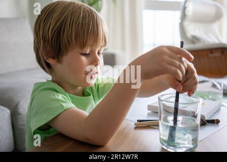 Giovane ragazzo dipingendo scritta verde decorativa su un sketchpad con un pennello e pittura a colori ad acqua. Foto Stock