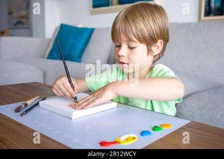 Giovane ragazzo dipingendo scritta verde decorativa su un sketchpad con un pennello e pittura a colori ad acqua. Foto Stock