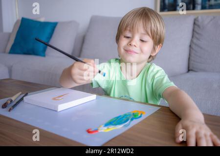 Giovane ragazzo dipingendo scritta verde decorativa su un sketchpad con un pennello e pittura a colori ad acqua. Foto Stock