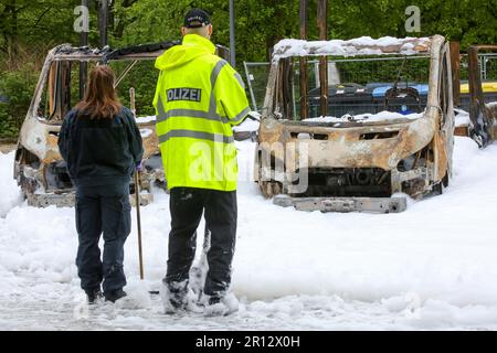 11 maggio 2023, Amburgo: Diversi furgoni di consegna bruciati si trovano nel parcheggio di un centro di distribuzione della posta ad Amburgo-Altona, Germania, che ha preso fuoco giovedì sera. La schiuma antincendio bianca può essere vista dall'operazione antincendio. Tre furgoni erano a fuoco pieno, due dei quali erano veicoli elettrici che il reparto antincendio doveva lasciare bruciare in modo controllato perché le loro batterie erano danneggiate, secondo un portavoce del reparto antincendio di Amburgo. La causa dell'incendio era inizialmente poco chiara. Tuttavia, una portavoce della polizia ha affermato che erano in corso indagini su sospetti Foto Stock