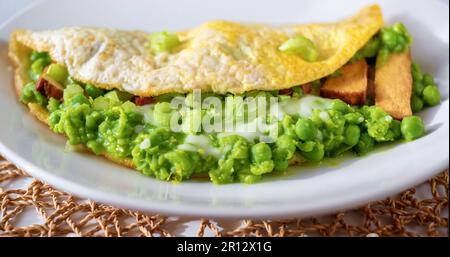 Omelette all'uovo con purè di piselli freschi, gambo di sedano e tofu affumicato su piatto bianco su tampone di bambù, primo piano. Foto Stock