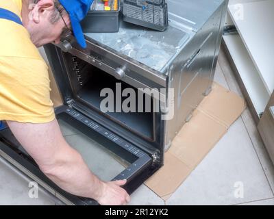 Addetto alla manutenzione che rimuove lo sportello del forno elettrico per facilitare l'accesso alle riparazioni Foto Stock
