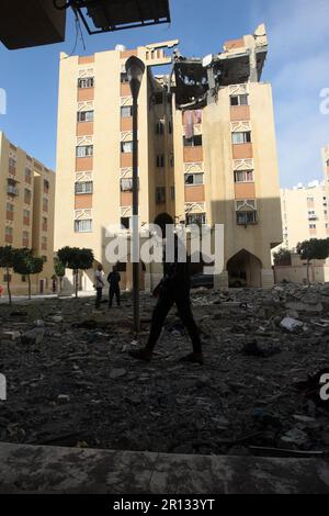 I palistiniani camminano tra i detriti oltre l'edificio che ospita l'appartamento (ultimo piano) di un leader militare della Jihad islamica, distrutto da uno sciopero aereo israeliano a Khan Yunis nella striscia di Gaza, il giorno 11 maggio 2023. L'esercito israeliano e i militanti di Gaza hanno commerciato un pesante incendio transfrontaliero durante la notte, con almeno 25 palestinesi uccisi in due giorni. Foto di Ismael Mohamad/UPI Credit: UPI/Alamy Live News Foto Stock