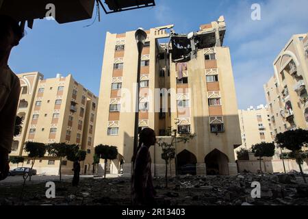 I palistiniani camminano tra i detriti oltre l'edificio che ospita l'appartamento (ultimo piano) di un leader militare della Jihad islamica, distrutto da uno sciopero aereo israeliano a Khan Yunis nella striscia di Gaza, il giorno 11 maggio 2023. L'esercito israeliano e i militanti di Gaza hanno commerciato un pesante incendio transfrontaliero durante la notte, con almeno 25 palestinesi uccisi in due giorni. Foto di Ismael Mohamad/UPI Credit: UPI/Alamy Live News Foto Stock