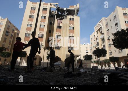 I palistiniani camminano tra i detriti oltre l'edificio che ospita l'appartamento (ultimo piano) di un leader militare della Jihad islamica, distrutto da uno sciopero aereo israeliano a Khan Yunis nella striscia di Gaza, il giorno 11 maggio 2023. L'esercito israeliano e i militanti di Gaza hanno commerciato un pesante incendio transfrontaliero durante la notte, con almeno 25 palestinesi uccisi in due giorni. Foto di Ismael Mohamad/UPI Credit: UPI/Alamy Live News Foto Stock