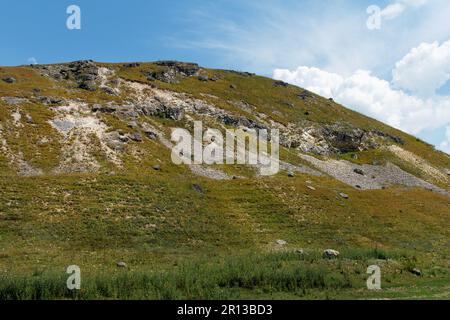 Fantastica vista dal basso della collina e delle nuvole in una giornata di sole. Erba e molte pietre crescono in collina. Piccole pietre versano giù in co non-tempo Foto Stock