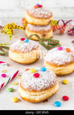 Carnevale ciambelle in polvere di zucchero rialzate con filoni di carta, confetti e chicchi di cioccolato su sfondo bianco, verticale Foto Stock