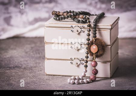 Collana con perle, bigiotteria, su una scatola di gioielli in legno bianco, colori grigio, bianco e rosa, sfondo grigio, stile vintage Foto Stock