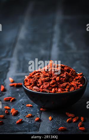 Ciotola con bacche di Goji essiccate, bacche di wolfberries cinesi, su fondo nero, verticale con spazio copia Foto Stock