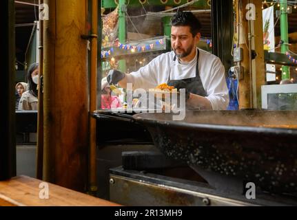 Londra, Inghilterra, Regno Unito. Borough Market, Southwark. Uomo cucinare e vendere paella Foto Stock