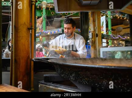 Londra, Inghilterra, Regno Unito. Borough Market, Southwark. Uomo cucinare e vendere paella Foto Stock