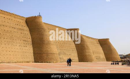 vista delle massicce mura e torri della cittadella dell'arca di bukhara torreggiante sui turisti in visita Foto Stock