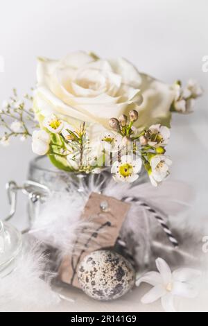 Rosa bianca e fiori primaverili in vaso di mason decorato con piume e uovo di quaglia, verticale Foto Stock