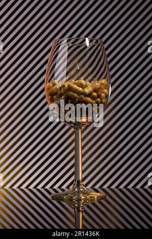 primo piano di un wineglass riempito di capsule e di uno sfondo con strisce dorate e ombre reali Foto Stock