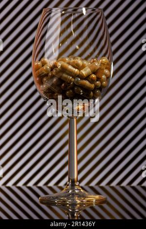 primo piano di un wineglass riempito di capsule e di uno sfondo con strisce dorate e ombre reali Foto Stock