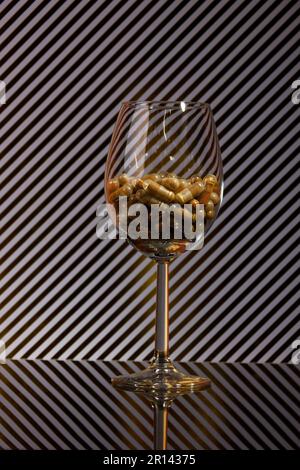 primo piano di un wineglass riempito di capsule e di uno sfondo con strisce dorate e ombre reali Foto Stock