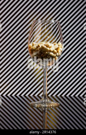 primo piano di un wineglass riempito di capsule e di uno sfondo con strisce dorate e ombre reali Foto Stock