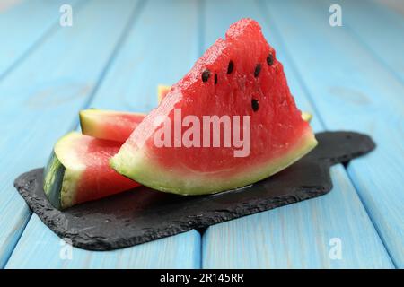 Tavola di ardesia con fettine di cocomero succoso su un tavolo di legno azzurro Foto Stock