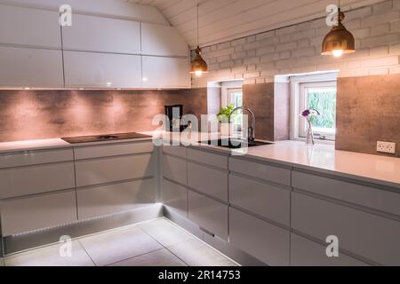 Moderno angolo cottura con piano di lavoro bianco, lavabo nero e lampade in metallo color rame, stile industriale Foto Stock