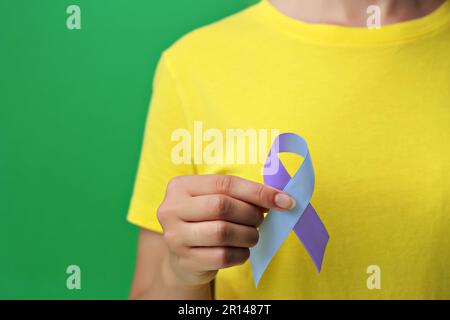 Giornata Mondiale dell'Artrite. Donna con nastro di consapevolezza blu e viola su sfondo verde, primo piano Foto Stock