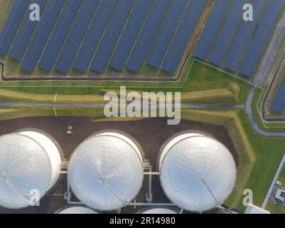 Scopri l'intersezione tra la produzione di energia tradizionale e la tecnologia rinnovabile con una splendida vista aerea dei silos di stoccaggio dell'olio e dei pannelli solari Foto Stock